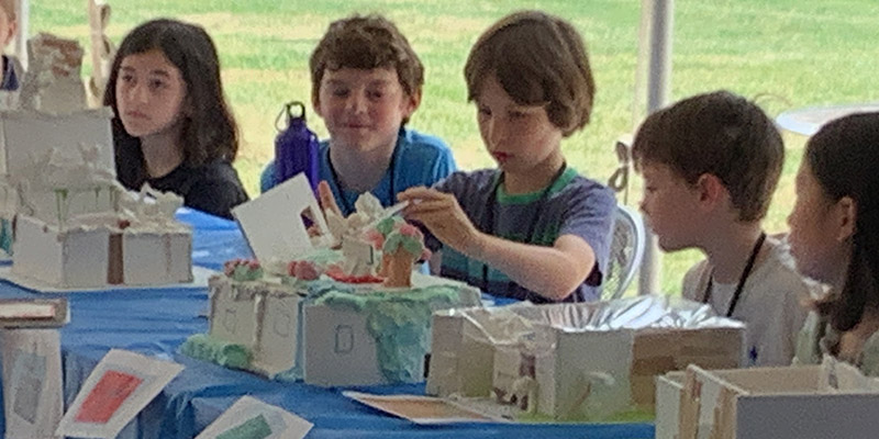 Five campers sit at a long table as the camper in the center presents his model