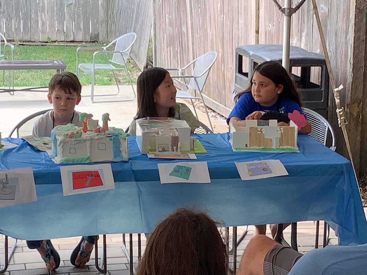 Three campers sit next to one another at the camp’s Friday Showcase, where campers get to present their models to family and friends