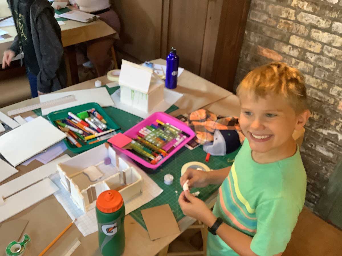 A young camper smiles while looking across the room as he works with modeling clay for his client’s model